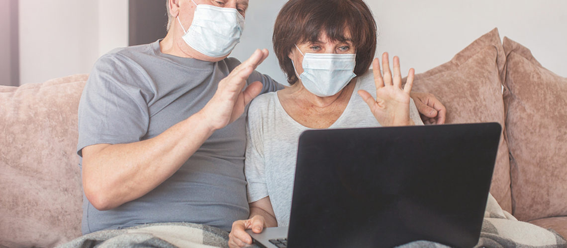 Couple old aged senior people at home with seasonal winter cold illness communicate online sit down on the sofa. Elderly couple in medical masks during the pandemic Coronavirus CoVid-19