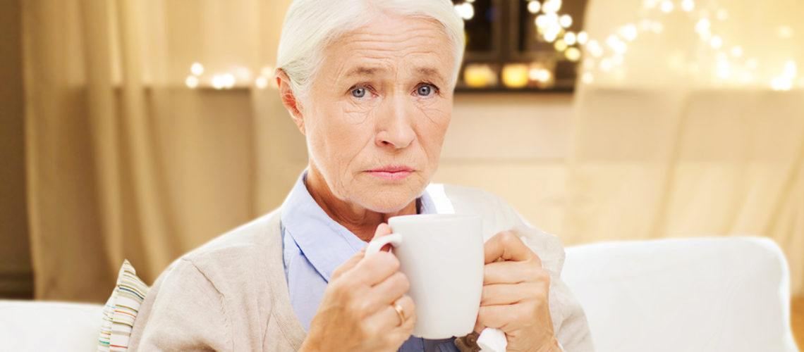 health, old age and people concept - sick senior woman suffering from flu or cold with paper napkin drinking hot tea at home over garland lights background